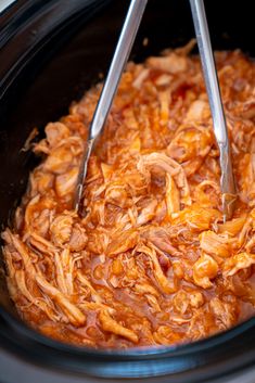 two tongs are in the crock pot filled with shredded meat