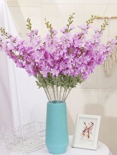 purple flowers are in a blue vase on a white table next to a framed photograph