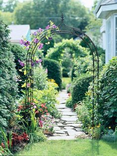 an arch in the middle of a garden with flowers growing on it's sides