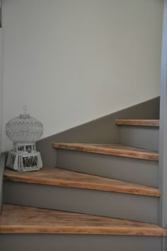 a white birdcage sitting on top of some wooden steps next to a wall