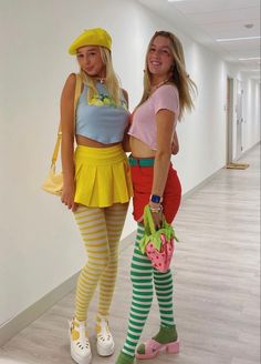 two young women dressed in costumes standing next to each other on the floor, one holding a handbag