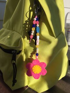 a yellow backpack with a pink flower and beads hanging from it's front pocket