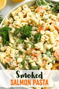 a white bowl filled with pasta and broccoli on top of a table next to lemons