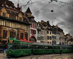 a green bus driving down a street next to tall buildings and power lines in the sky