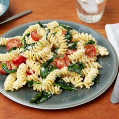 a plate of pasta with spinach, tomatoes and cheese on it next to silverware