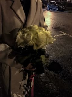 a man in a suit holding a bouquet of flowers on the side of the road