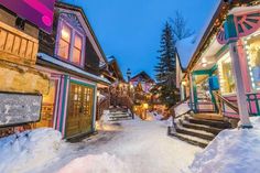 a snowy street lined with wooden buildings and steps leading to the storefronts at night