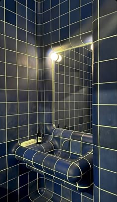 a bathroom with blue tiled walls and yellow lights on the mirror, along with a bench