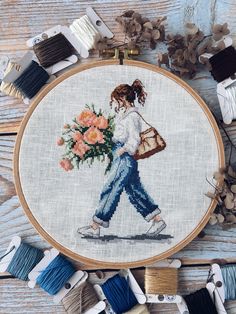 a cross stitch pattern with a woman carrying flowers in her hand, surrounded by spools of thread