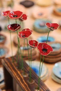 three red flowers are in a vase on a table with other plates and bowls behind it