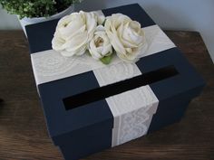 two white roses sitting on top of a black and white gift box with lace trim