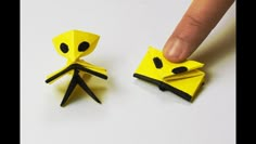 someone is pointing at the yellow origami piece that looks like a person's head