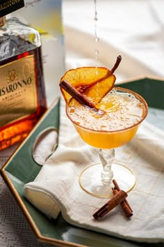 a drink in a glass on a tray with cinnamon and an orange peel garnish