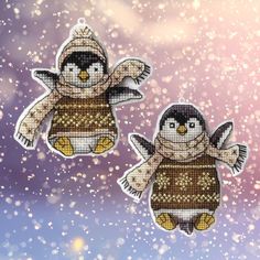 two penguins wearing winter clothes hanging from strings