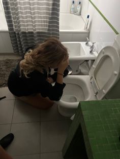 a woman sitting on the floor in front of a toilet with her hands to her face