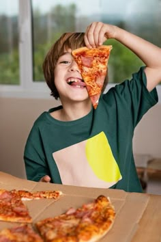 a young boy holding up a slice of pizza to his face