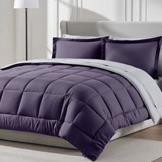 a bed with purple comforter and pillows on it