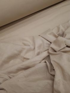 an unmade bed with white sheets on top of it and a rolled up pillow