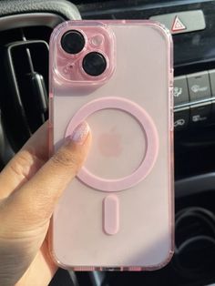 a person holding up a pink phone case with an iphone in the middle and a car steering wheel behind them