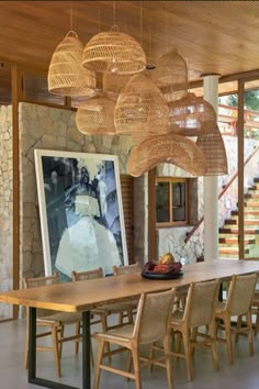 a dining room table and chairs in front of a painting on the wall with hanging lights above it