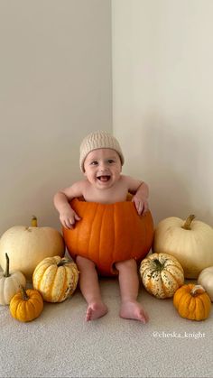 a baby sitting on top of a pumpkin surrounded by smaller pumpkins