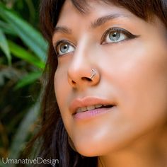 a woman with piercings on her nose looking off to the side in front of some plants