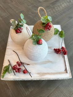 two white vases with red berries and green leaves on a wooden tray next to each other