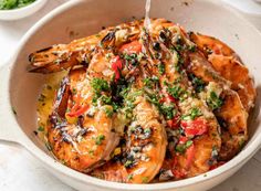 a white bowl filled with cooked shrimp and garnished with parsley