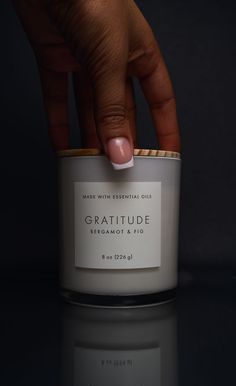 a person's hand holding onto a candle with the word, gratitude bergamot & fig on it