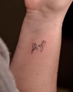 a small tattoo on the wrist of a woman's left arm, with two birds flying above it