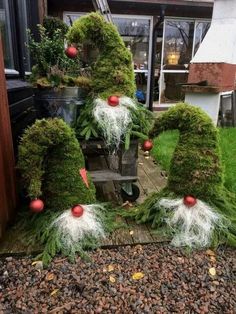 three gnomes made out of grass with red and white balls on their heads, sitting in front of a house