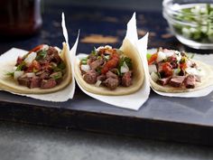 three tortillas with meat and vegetables are on a tray next to a bowl