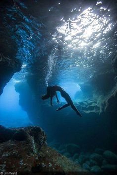 a person swimming in the water near rocks and rock formations, with sunlight coming through