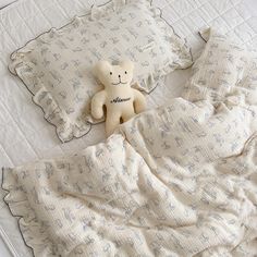 a teddy bear laying on top of a bed under a white comforter and pillows