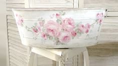 a white bucket with pink flowers painted on it sitting on top of a wooden stool