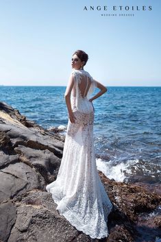 a woman standing on top of a rocky beach next to the ocean wearing a white dress