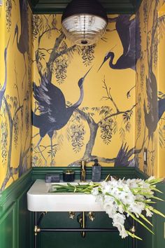 a bathroom with yellow and green wallpaper, white sink and floral arrangement on the counter