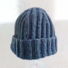 a blue knitted hat sitting on top of a white headphone holder with an ear cord