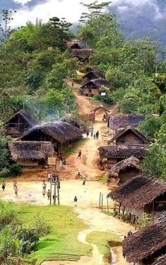 a dirt road that has some huts on top of it and people walking down the path