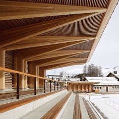 a wooden building with snow on the ground and buildings in the background that are covered by wood slats