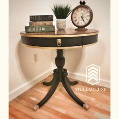 a table with a clock, books and plant on it in front of a wall