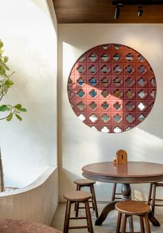 a wooden table sitting under a round window next to two stools and a potted plant