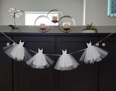 three white dresses hanging from a line on a string in front of a dresser with candles and flowers