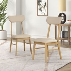 two beige chairs sitting on top of a rug in front of a white wall and floor