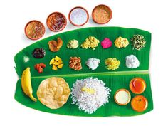 a banana leaf with different types of food on it and some dipping sauces in bowls