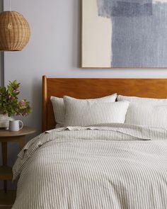 a bed with striped sheets and pillows in a room next to a painting on the wall