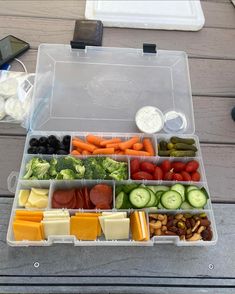 a plastic container filled with lots of different types of vegetables and cheeses on top of a wooden table