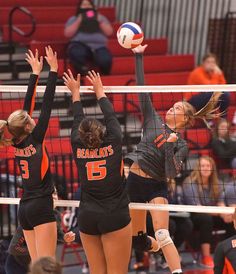 three girls playing volleyball in the middle of a game, with one jumping up to hit the ball