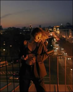 a woman looking at her cell phone while standing on a balcony overlooking the city lights