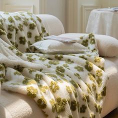 a white couch with a green and yellow blanket sitting on it's back next to a pillow